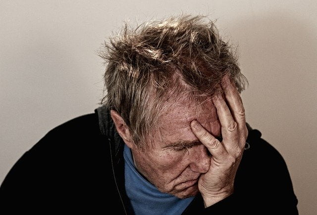 Old man holding his head looking tired at a drug and alcohol rehab in Luton