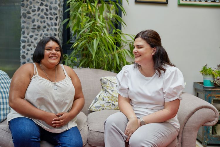 Two women smiling and sitting on a sofa