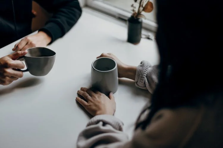 Two people drinking coffee and facing each other at a table