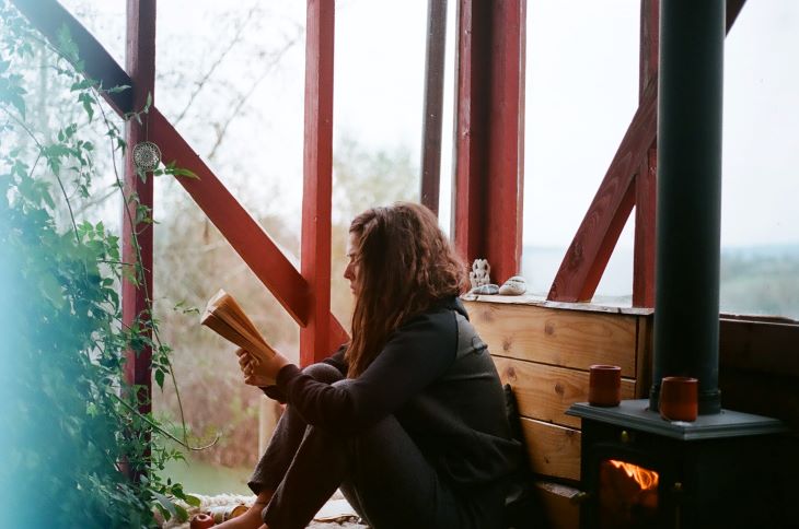 Woman reading a book next to a fire at a drug and alcohol rehab centre in Norfolk