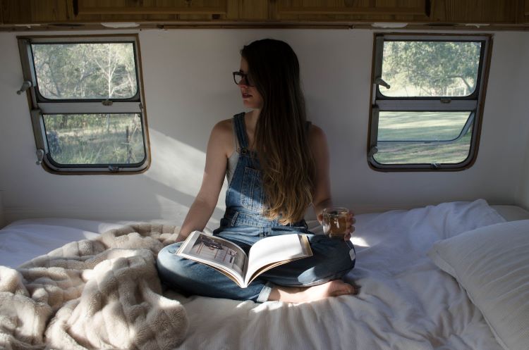 A woman reading a book, cross-legged in bed.