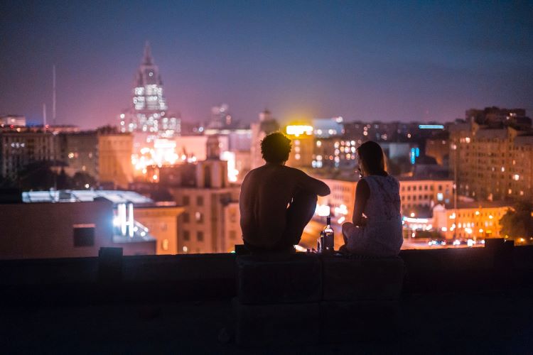 Two people with an alcohol bottle looking at the night city skyline