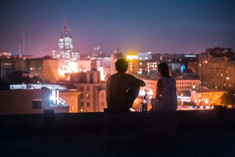 Two people with an alcohol bottle looking at the night city skyline