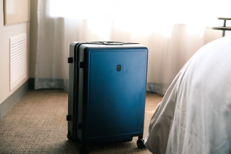 A blue suitcase beside a bed