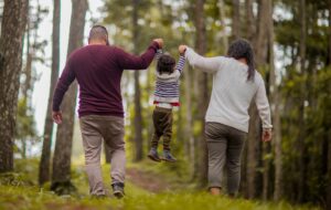 Father and mother swinging toddler between them as they walk through a forest