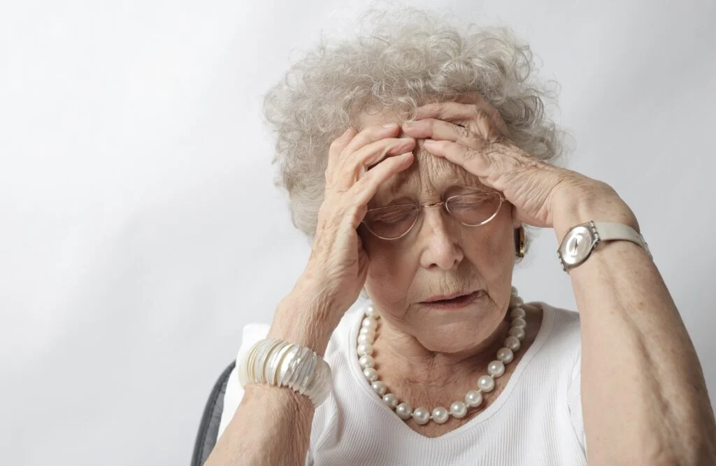 An old woman holding her head in distress suffering from alcoholism and vertigo