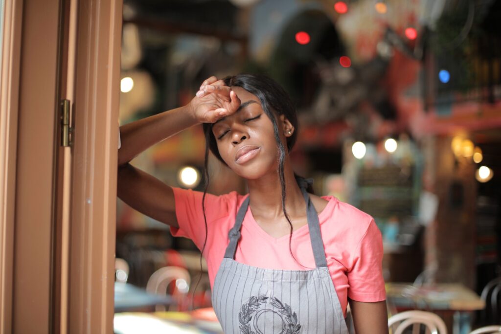 Woman wearing an apron looking tired and leaning against the wall in a coffee shop in Somerset