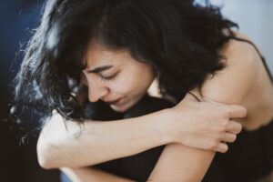 Woman sitting hugging her legs and looking distressed.