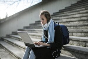 Woman wearing headphones sitting on some outdoor steps on her laptop