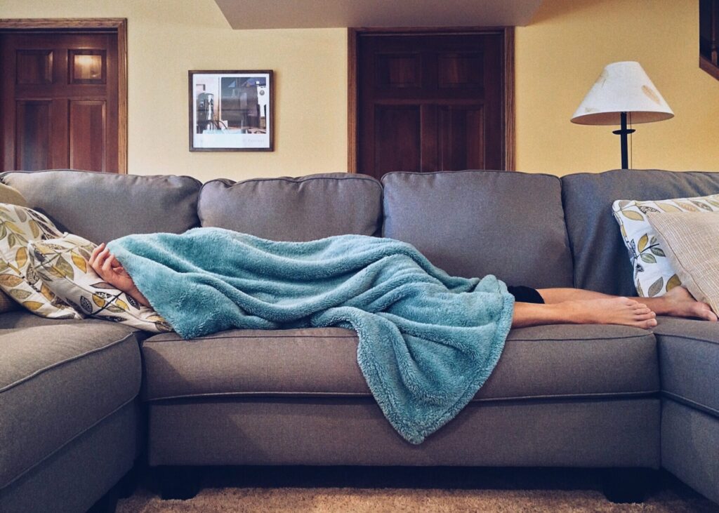 person lying on sofa with blanket