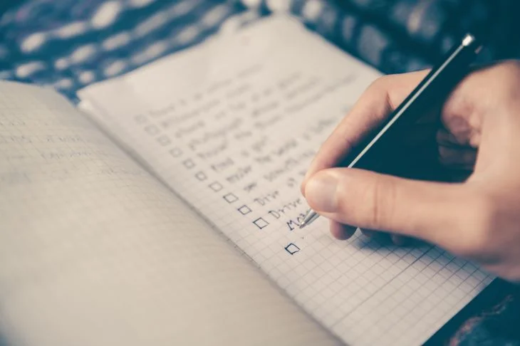 A person writing a checklist in a jotter